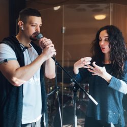 Musical teacher coaching a young male vocalist as he sings into a microphone during class at a music academy